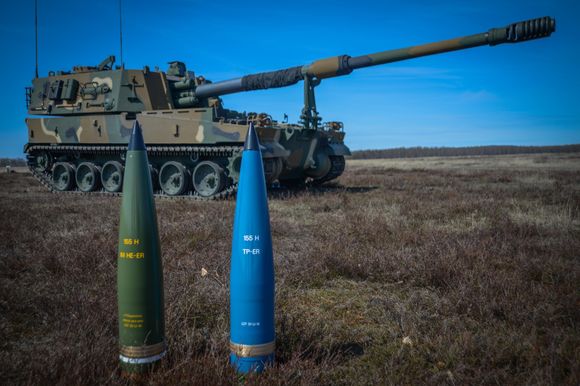 Den nye IM HE-ER-granaten og en treningsversjon (blå) foran ei K9-vogn. Finland er første bruker av ammunisjonen i det koreanskbygde artilleriet som også er en kandidat i Norge. <i>Bilde:  Nammo</i>