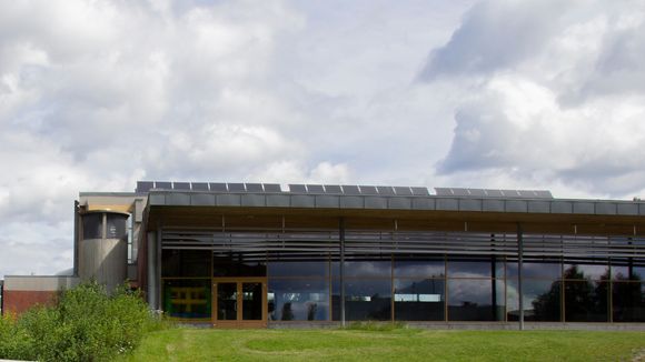 Nadderudhallen har solfangere på taket. Tilknyttet hallen (t.v.) står en av tre energisentraler som skal forsyne området med varme fra gropvarmelageret som mulig bygges på fotballbanen som ligger til venstre utenfor bildet. <i>Foto:  Tuva Strøm Johannessen</i>