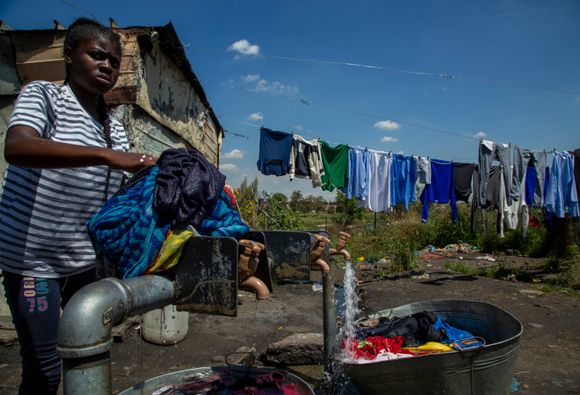 En kvinne vasker klærne under en kran i Soweto, Sør-Afrika. Koronaviruset truer nå de 1,3 milliarder menneskene som bor i Afrika. <i>Foto:  AP</i>