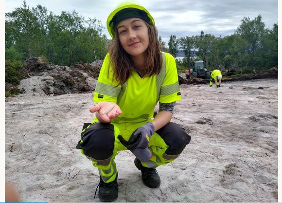 Arkeolog Martine Lahti viser fram en av pilspissene som er funnet i veitraseen. <i>Foto:  Universitetet i Tromsø</i>