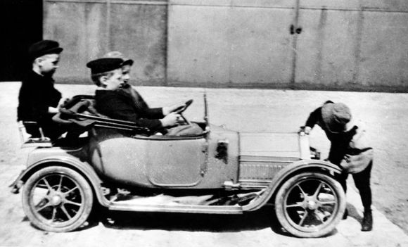 Denne lille Cadillac-elbilen er faktisk kongehusets aller første elbil. Kronprins Olav fikk den i julegave av dronning Alexandra av England. Her sitter han selv bak rattet og er sammen med tre kamerater. <i>Foto:  NTB</i>