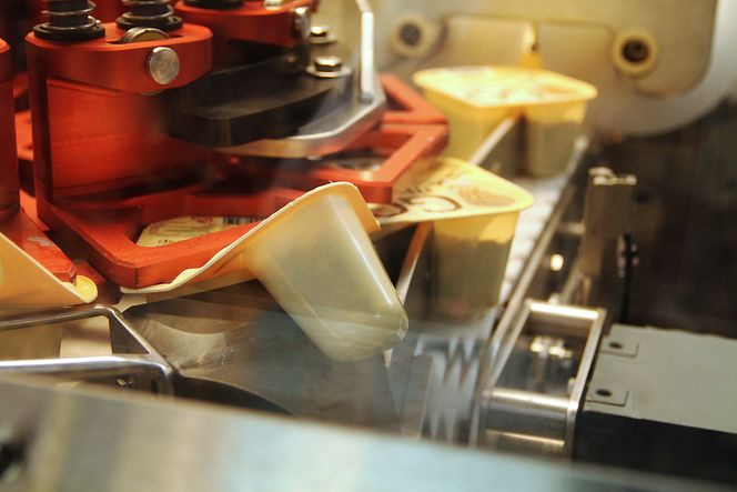 Den røde skiven fører yoghurtbegrene slik at de to delene blir brettet fra hverandre, og skje kan limes på. Systemet er utviklet av Skala Maskon og Omron.