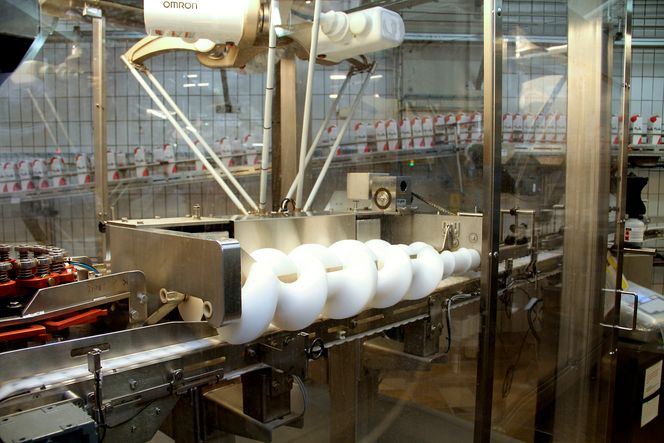 Øverst Omrons nye deltarobot som løfter ferdige yoghurtbegre over i kartonger. Nederst i bildet en skrue som snur begrene 180 grader, i riktig posisjon for å få limt skjeene. Den er tatt med fra den opprinnelige løsningen fordi den har vist seg å være en suksess.