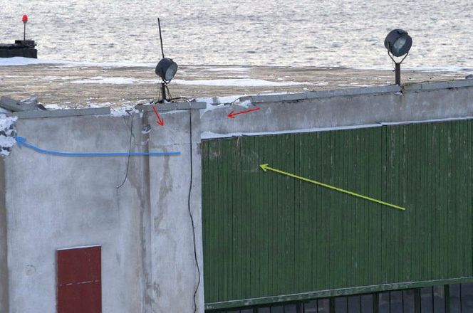 Treffpunktet oppe på det sydlige (venstre) hjørnet av hangaren. Grønn pil indikerer retningen helikopteret kom, og røde piler viser blå fargeavsetning på betongen. Ettersammenstøtet fortsatte helikopteret til venstre som antydet med blå pil.