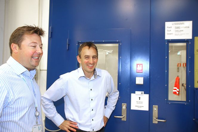 Trykket: Bak den blå døren er det 18 trykkceller der utstyr kan testes ned til 350 bar. Selve rommet er ikke under trykk, men utstyret som skal trykktestes monteres i jigger med olje under trykk. Det reduserer faren dersom noe går galt, forteller Espen Bostadløkken og Bjørn Rasch. Foto: Tore Stensvold