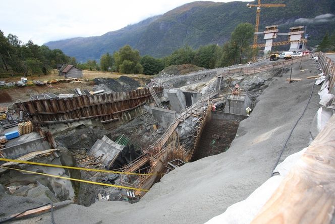 SPREDEKAMMER: I denne byggegropen forberedes spredekammeret. Midt i bildet er de to spredesalene. Mannen på høyre sadel arbeider med en laser for å finjustere strekkfiskene før den siste forankringsklossen blir støpt. Nederst til venstre i bildet er den andre og ferdigstøpte forankringsklossen. Øverst til høyre er brotårnene, som nå har passert 120 meters høyde.
