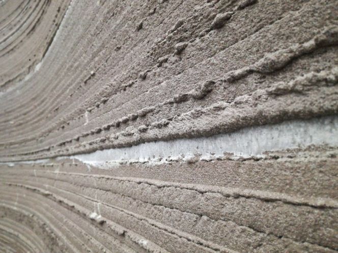 Det er lett å se lagdelingen i veggene. Og flere steder henger det girlandere av betong som vitner om at det har vært veldig vanskelig å styre konsistensen til betongen underveis i skriveprosessen. Den viktigste årsaken til problemet er at gruppen valgte å bruke nedknust tegl som tilsetning. Og siden teglsteinen suger fukt fra omgivelsene, er det svært vanskelig å dosere mengden av tilsatt vann korrekt. Derfor har det under hele utskriftsprosessen sittet en person og holdt øye med bildene fra de kameraene som er montert på skriverhodet, så han kunne gi den som var ansvarlig for å blande betongen beskjed om å justere vannmengden i blandingen. (Foto: Ulrik Andersen)