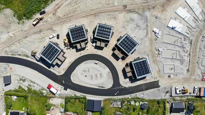 Fra oven kan man se solcellepanelene som speiler seg i sola. De sørger for mer strøm enn boligene har bruk for. Og da har man lagt inn som forutsetning at de som bor her har elbil. Foto:  Eirik Helland Urke