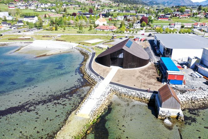 Miljøbygg: Vikingsenteret Sagastad er etablert i det runde, brune bygget. Vekslerhuset der fjordvarmen kommer inn ligger i forgrunnen. Legg merke til solcelleanlegget på taket som gjør Sagastad-bygget tidvis selvforsynt med energi. Foto: Jørn-Arne Tomasgaard