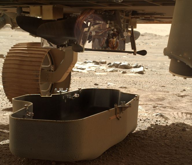 Her er beskyttelseslokket over Ingenuity akkurat sluppet ned fra buken på Perseverance. Vi kan så vidt skimte helikopteret ligge vannrett oppunder roveren. Foto:  NASA