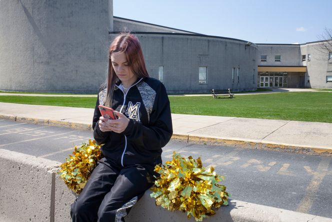 Brandi Levy poserer med mobiltelefon og cheerleader-antrekk utenfor sin gamle high school. Foto: Danna Singer/ACLU/AP/NTB