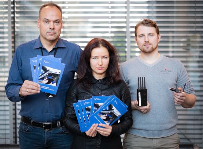 Brosjyrene skal informere sjåfører som passerer grensen om at jammere er forbudt i Norge. Nkoms avdelingsdirektør (fra v.) Per Eirik Heimdal og senioringeniør Nataliya Kovalevska som viser brosjyrene, mens overingeniør Nicolai Gerrard viser to typer jammere. Foto: Cato Berge, Nkom