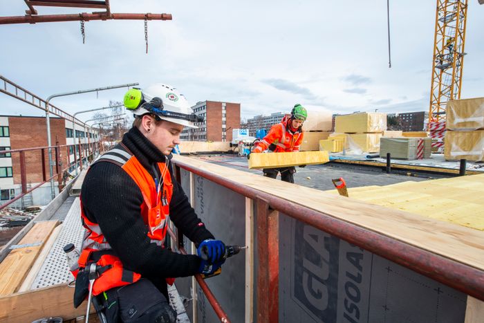 Tømrerlærling skrur mens BAS Magnus Lunder legger GLAVA® Robust på det nesten ferdige taket. <i>Foto:  Paal-André Schwital</i>