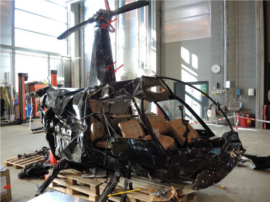Skadene på helikopterets høyre side fotografert i Havarikommisjonens hangar. Røde piler peker påområder med smeltet aluminium. Gul pil peker mot skrapemerker på høyre fremre undersellslegg. Foto: SHK