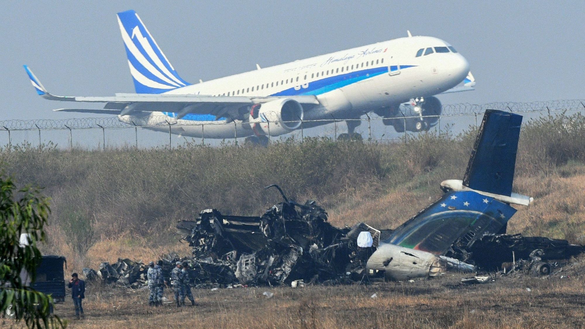 Det utbrente Q400-vraket ligger utenfor rullebanen i Katmandu med et A320 fra Himalaya airlines i bakgrunnen.