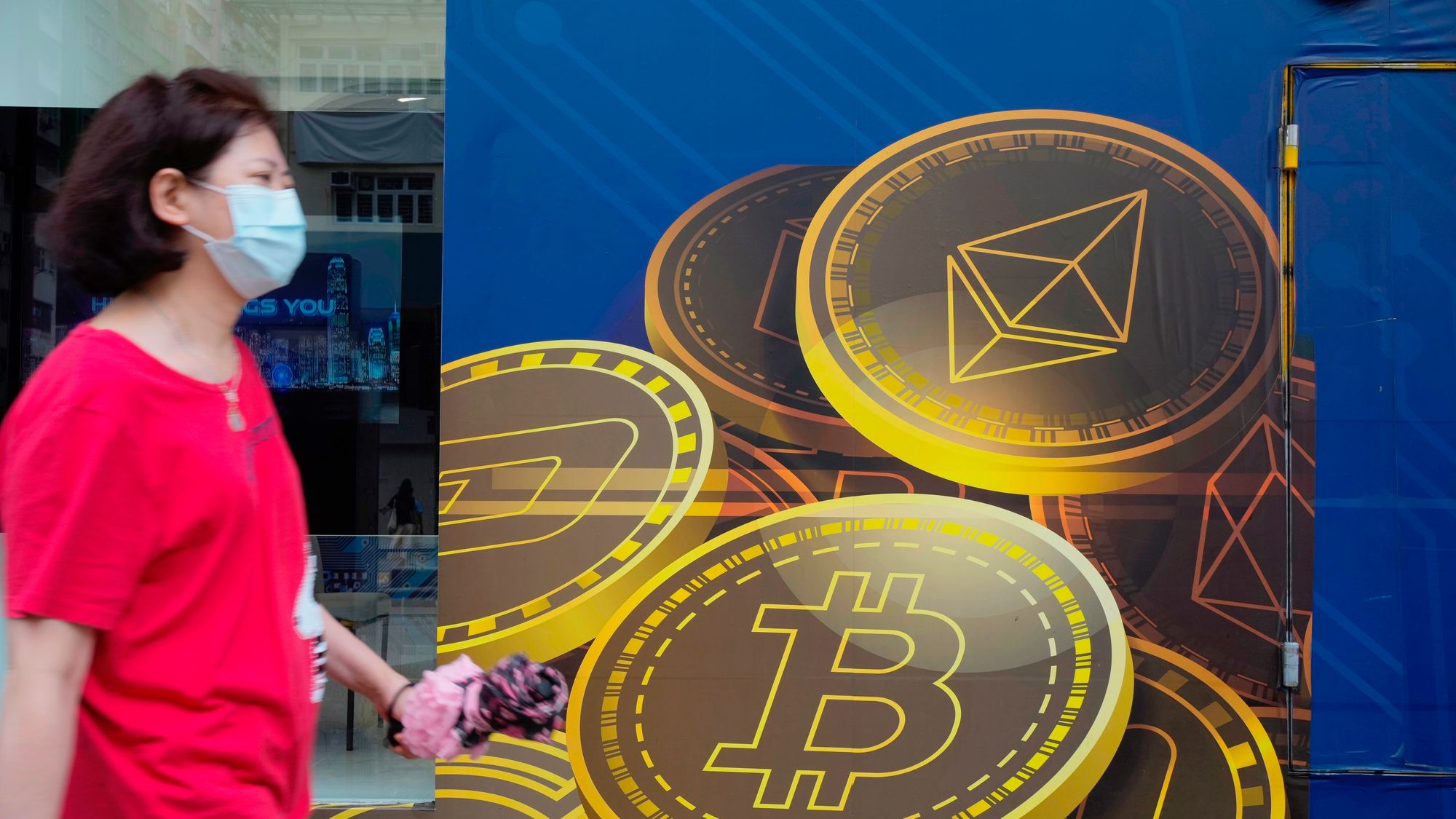 En kvinne passerer reklame for kryptovalutaen bitcoin i Hongkong. Utvinning av bitcoin krever enorme mengder energi er og er businessen er blitt en miljøversting.