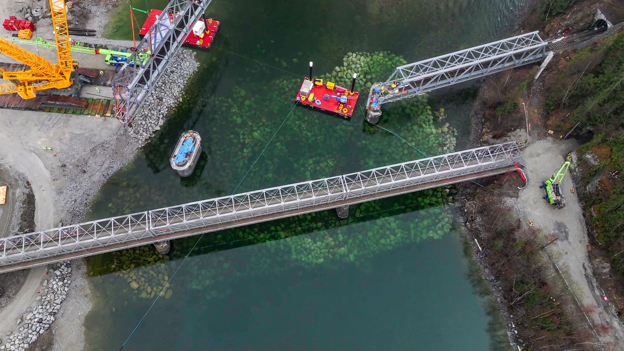 Jernbanen er ment å være klimavennlig. Nå trues den av ras, flommer og ekstremnedbør som følge av menneskeskapte klimaendringer. Bildene viser bruelementer som løftes på plass igjen etter at ekstremværet «Hans» rev med seg Randklev bru ved Ringebu i 2023.