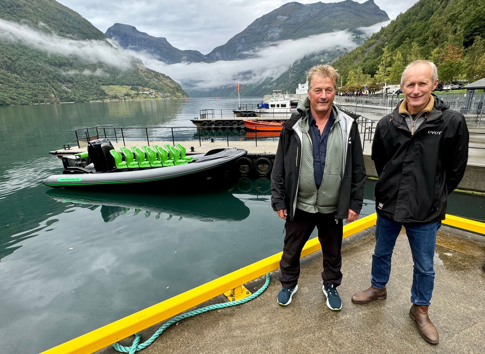 Frank Bonsaksen (t.v.) driver sightseeing i Geirangerfjorden. Her med den gjennomprøvde elbåten i bakgrunnen. Her sammen med Trond Strømgren fra motorleverandør Evoy.