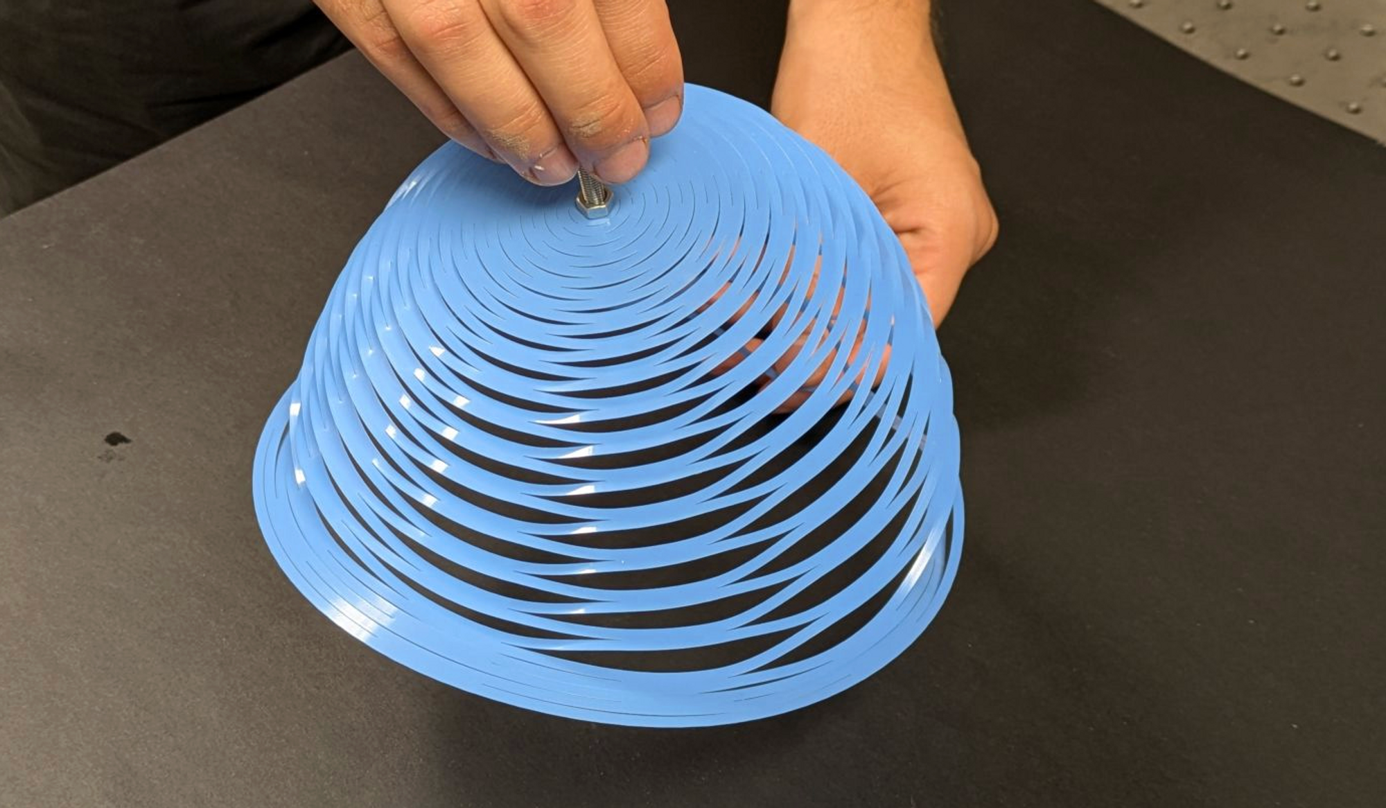 Her er den nye kirigami-inspirerte fallskjermen, hvor lasten er festet til midten av den originale flate skiven, der den øverste hånden er på dette bildet. Under et fall bidrar tyngdekraften til å folde ut fallskjermen, noe som gir den den store åpningen oppover.