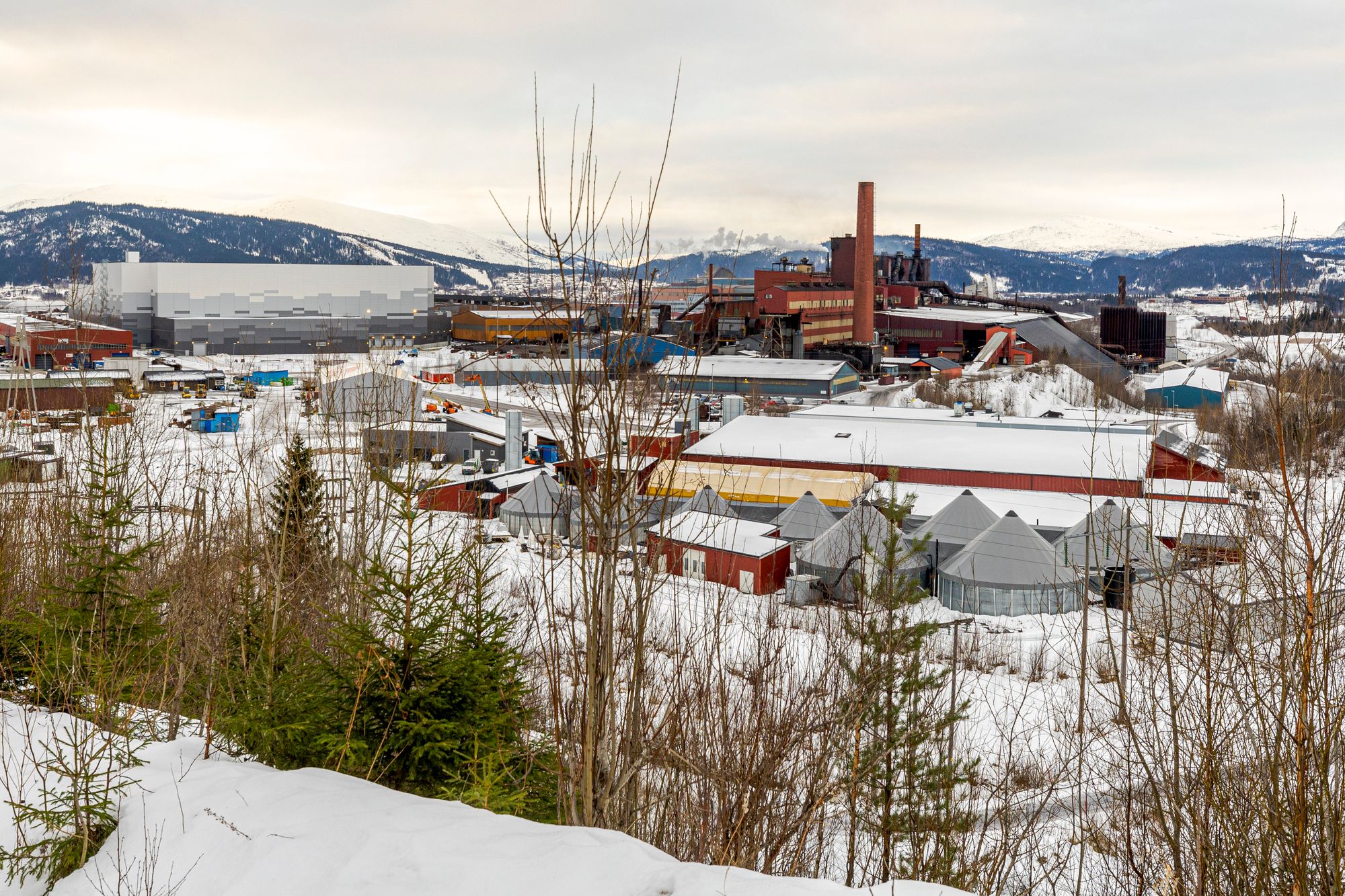 I Mo i Rana ligger gammel og ny industri side ved side. Det moderne bygget til venstre er Freyrs batterifabrikk, som selskapet vil selge til datasenter. 