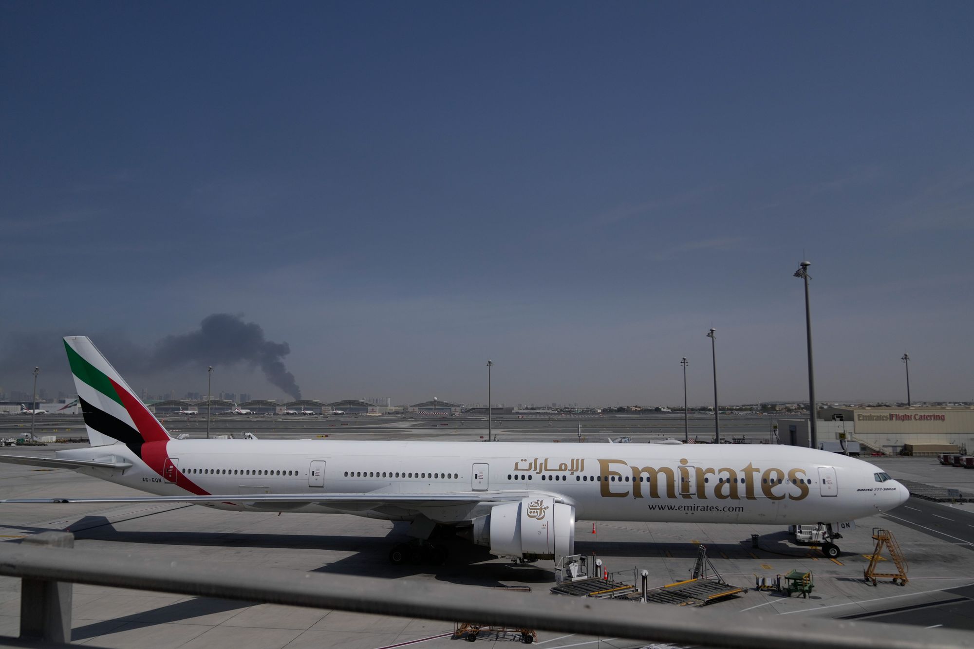 Et Emirates-fly på flyplassen i Dubai med røyk fra et iransk angrep i bakgrunnen.