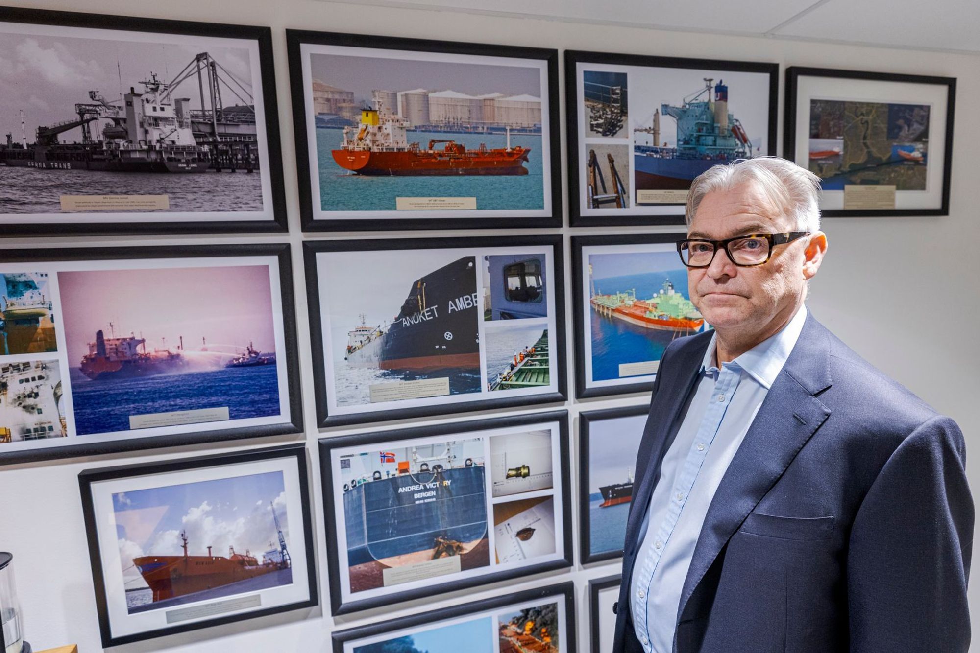 Svein Ringbakken er daglig leder i Den norske krigsforsikring for skib (DNK). Her står han foran en vegg med bilder fra kritiske situasjoner deres medlemmer har vært involvert i. 